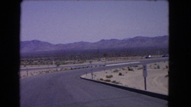 1966: a large highway with cars driving through the desert with mountains all