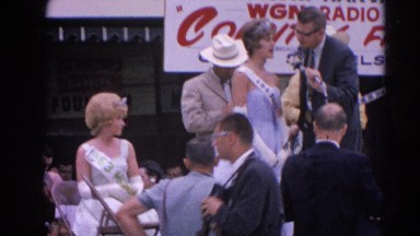 1964: a woman wearing a sash on stage with two men in a beauty pageant RACINE
