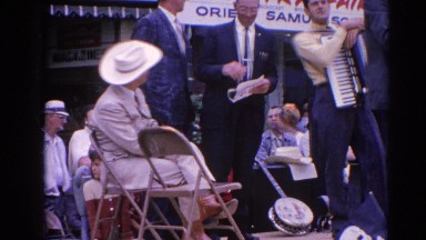 1964: a man with an accordion on a stage at a country fair with other men