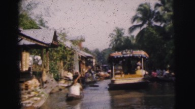 1962: people in boats paddling down a river within a community. DARJEELING