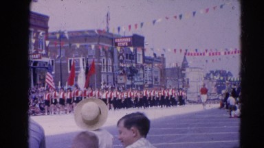 1964: Marching Band Performing in Parade Walking Down Street in Harvard, Illinois