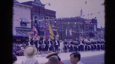 1964: people lined up on the street to watch a parade on a clear day. HARVARD