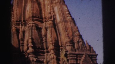 1962: brown monkey is climbing down ornate and ancient building facade. BANGKOK