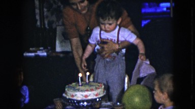 1951: Mother Helping Two Year Old Boy Blow Out Candles at Birthday Party