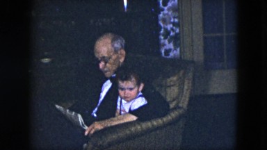 1951: a grandfather reading the newspaper to his young grandson in a chair