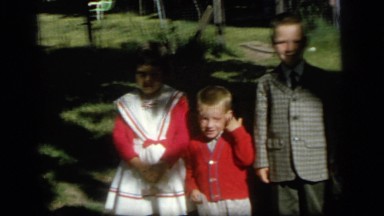 1964: three kids in sunday dress clothes pose for a photo in their yard. CAMDEN