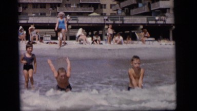 1964: children play in a body of water on a sunny day with lots of people