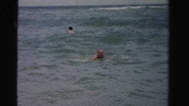 1955: old guy wearing yellow trunks happily swims through the waves of the ocean