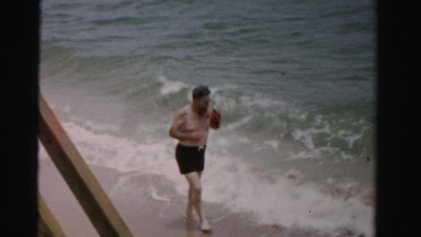 1955: an old man in black trousers walking along the beach MIAMI, FLORIDA