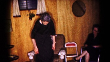 1961: group of men and women in dark clothes, woman straightens her dress
