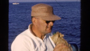 1958: old man drinking bottle of alcohol while motor boating on the open sea