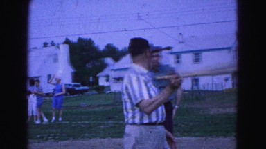 1964: older men outdoor playing baseball in the yard as people watch