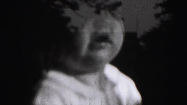 1946: baby playing near window with towering building reflected in the glass