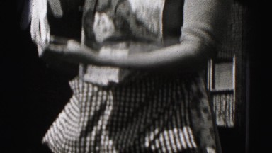 1946: woman lifts long glove while wearing floral apron under clothespin apron