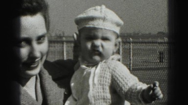 1946: baby in crocheted white outfit is held by mother