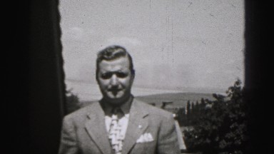 1946: man in suit and tie walks up to the camera and lifts his eyebrows