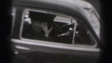 1946: an older female waving goodbye as the car pulls off down the street.