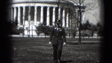 1946: policeman is walking toward the camera with building in the back