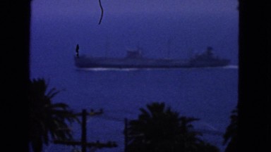 1963: boat or submarine cruises on water near palm trees and telephone lines