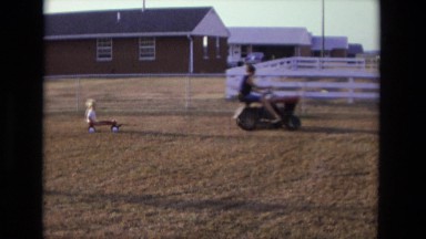 1975: woman on lawn mower pulling child in wagon behind her CALIFORNIA