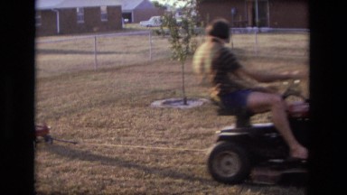 1975: dad riding lawn mower tractor pulling son in small red wagon CALIFORNIA