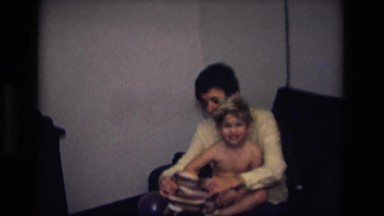 1975: caucasian woman putting striped long sleeved shirt onto small young boy