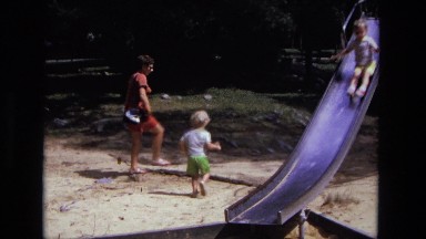 1975: child running while his mother follows behind on sunny day at the park.