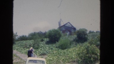 1962: house sits on hill as two people talk near car on the road SAN PEDRO