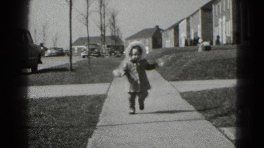 1947: Toddler Walks Down Sidewalk Wearing Mittens in Winter Suburb