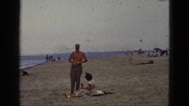 1953: man removes his pants at the beach showing his trunks. CALIFORNIA