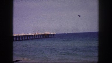 1960: the view of pier as the ocean crashes into the beach; two women posing