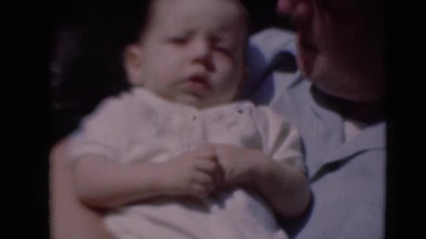 1947: proud dad holding baby boy moving son into shade out of bright sunshine