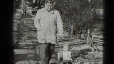 1947: man is using one hand to push stroller with kid in it along the sidewalk