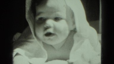 1947: baby with towel in sun after bath showing hand of caregiver
