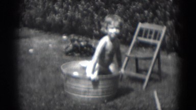 1949: small child cools off inside metal bucket full of water on hot summer day.
