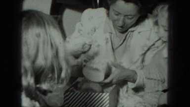 1949: smiling mother opening birthday present at party attended by family