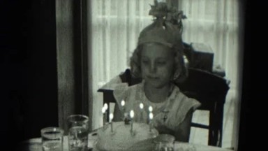1951: little girl attempting to blow out the candles on her birthday cake.