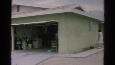 1966: woman in front of simple home using garden hose to water plants CALIFORNIA