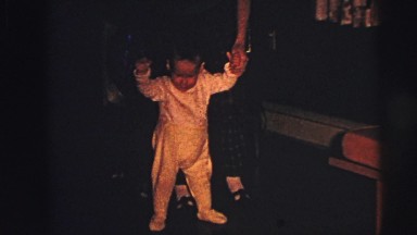 1973: mischievous kid held by his mother walking in the room, LYNBROOK, NEW YORK