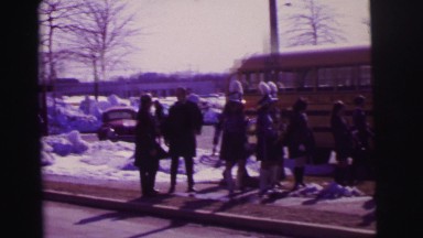 1974: children waiting at bus stop in cold winter snow weather LYNBROOK