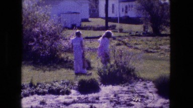 1976: two young blonde, dressed up girls looking into bushes around farmland