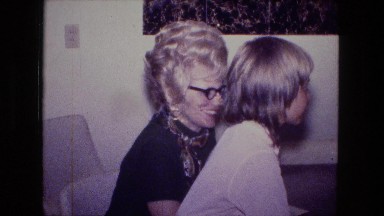 1976: middle aged women with blonde curly hair blowing out birthday candles cake