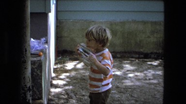1976: Old Home Video of Young Blonde White Boy in Striped Shirt Licking His Toy