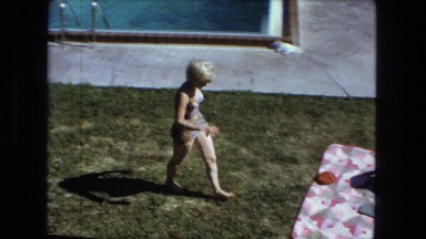 1976: two women sunbathing outdoor on blanket on the grass by the pool.