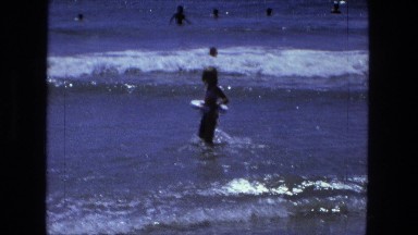 1976: young girl wading out into water with floatation device light waves