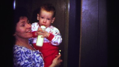 1973: bedtime for baby as cheerful mother carries him to bed while waving