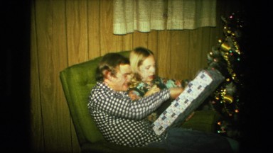 1974: young couple sit together in single green chair to open christmas presents