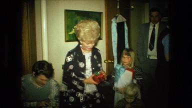 1974: woman holding red present surrounded by her family on christmas.