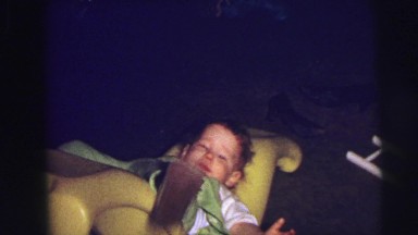 1973: baby falling over playing on yellow banana rocking chair LYNBROOK