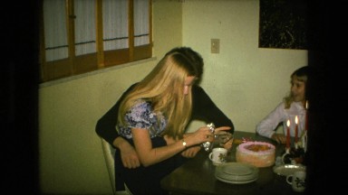 1974: woman sitting together with her family at table on her birthday opening